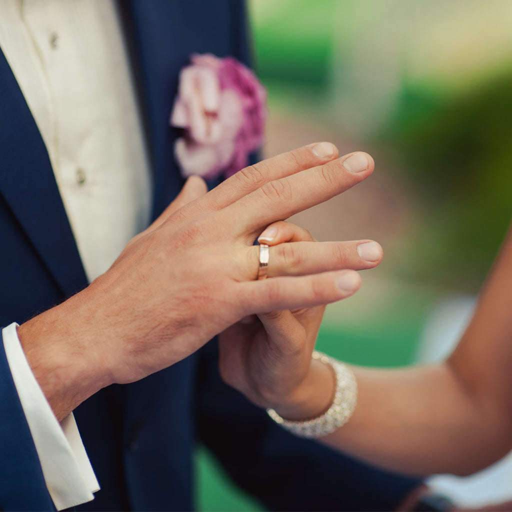 Bride putting wedding band on grooms hand.