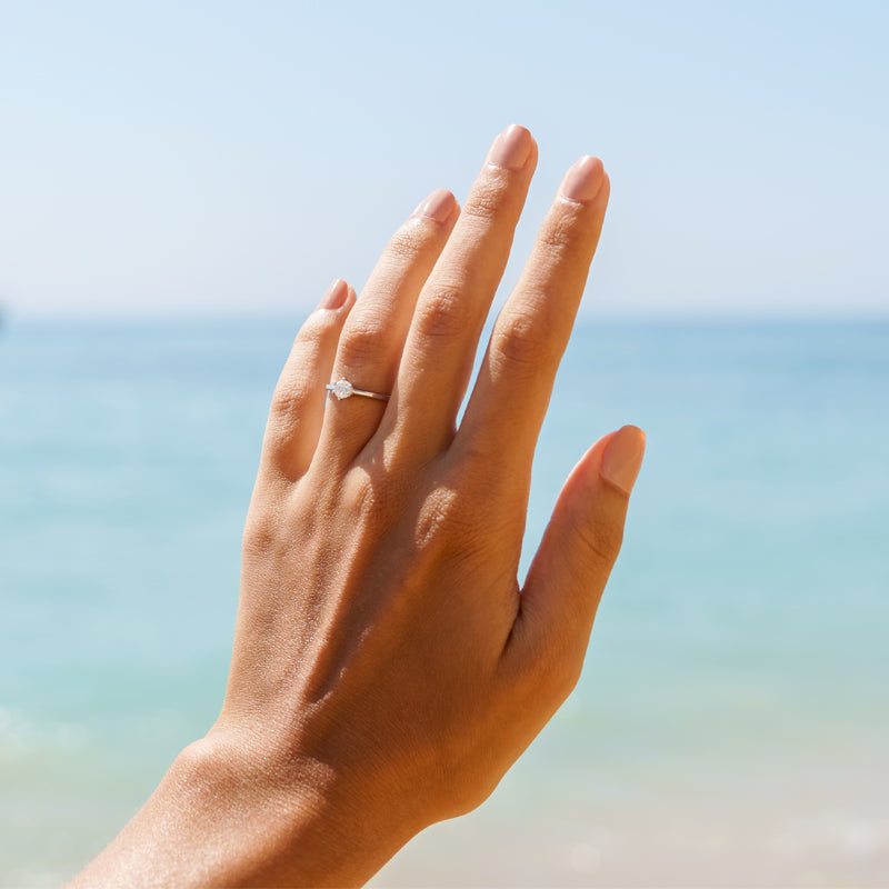 Ladies hand with engagement ring with the beach in the background.